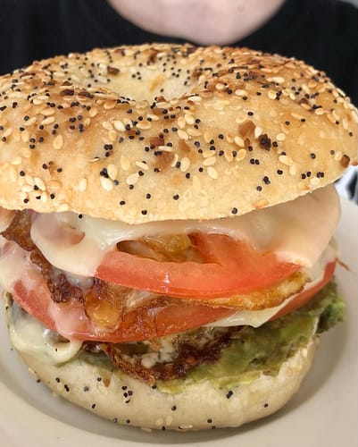 bacon egg and cheese with avocado and tomato on an everything bagel